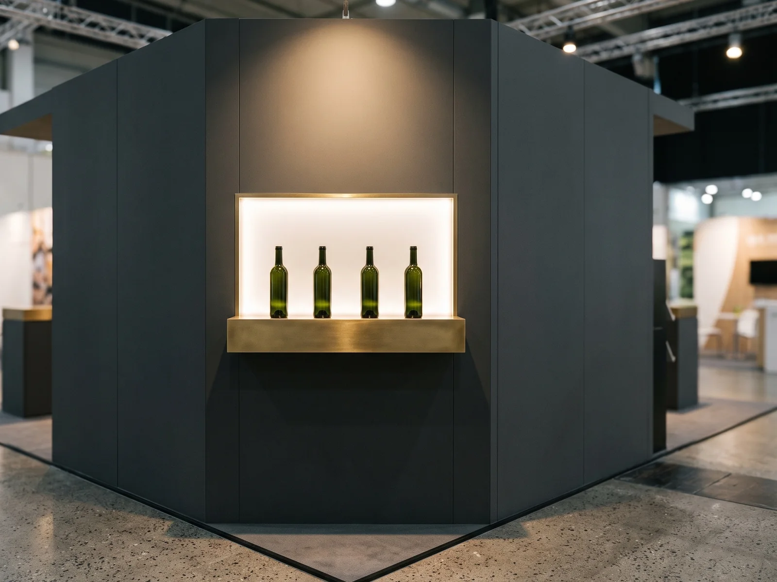 Minimal European food trade exhibition stand with brass shelf holding unlabelled dark green bottles